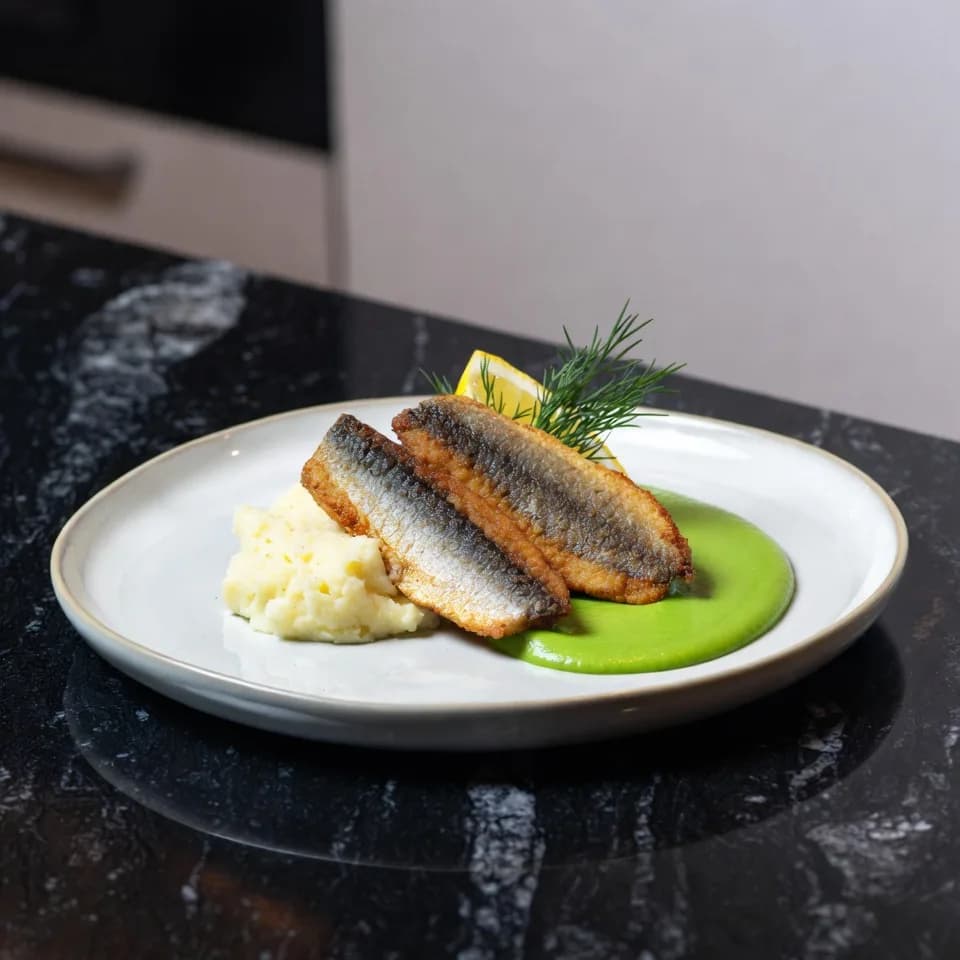 Stekt strömming med blomkålsmos och ärtpuré på en tallrik